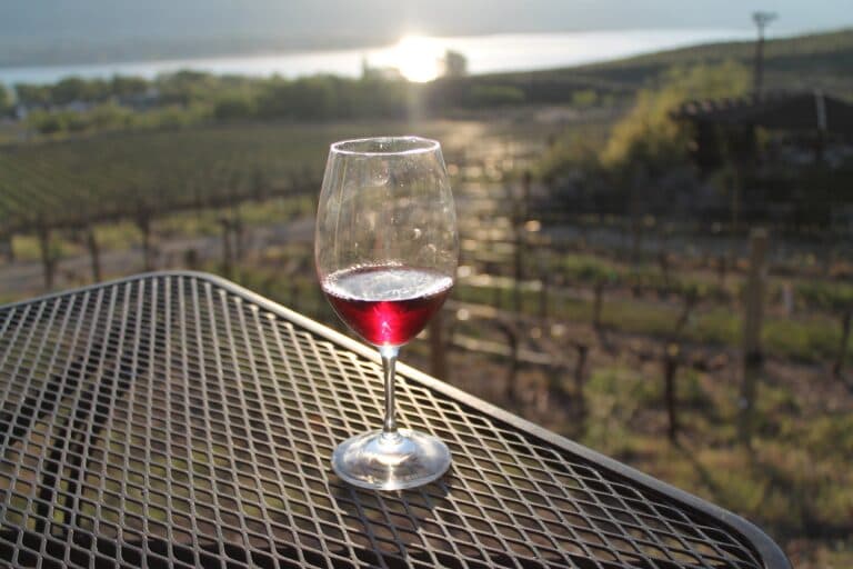A glass of red wine on a patio table overlooking the Osoyoos vineyards and lake at golden hour